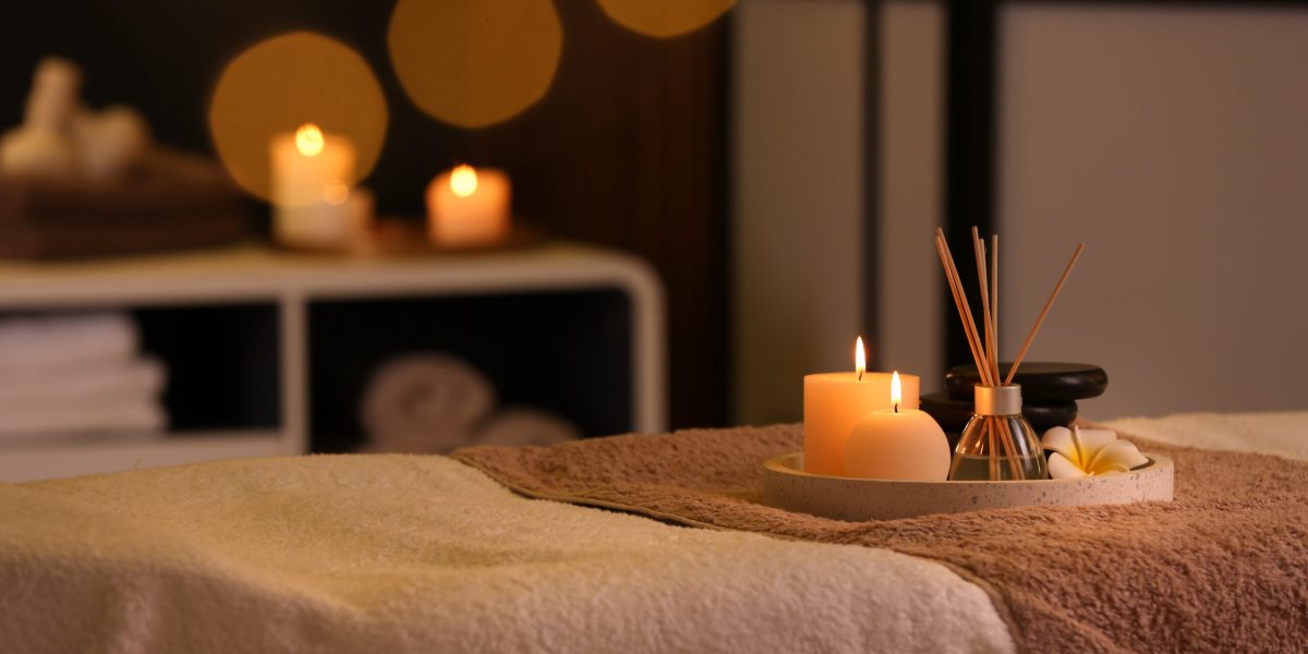 Burning candles and aromatic reed freshener on table in spa salon, space for text